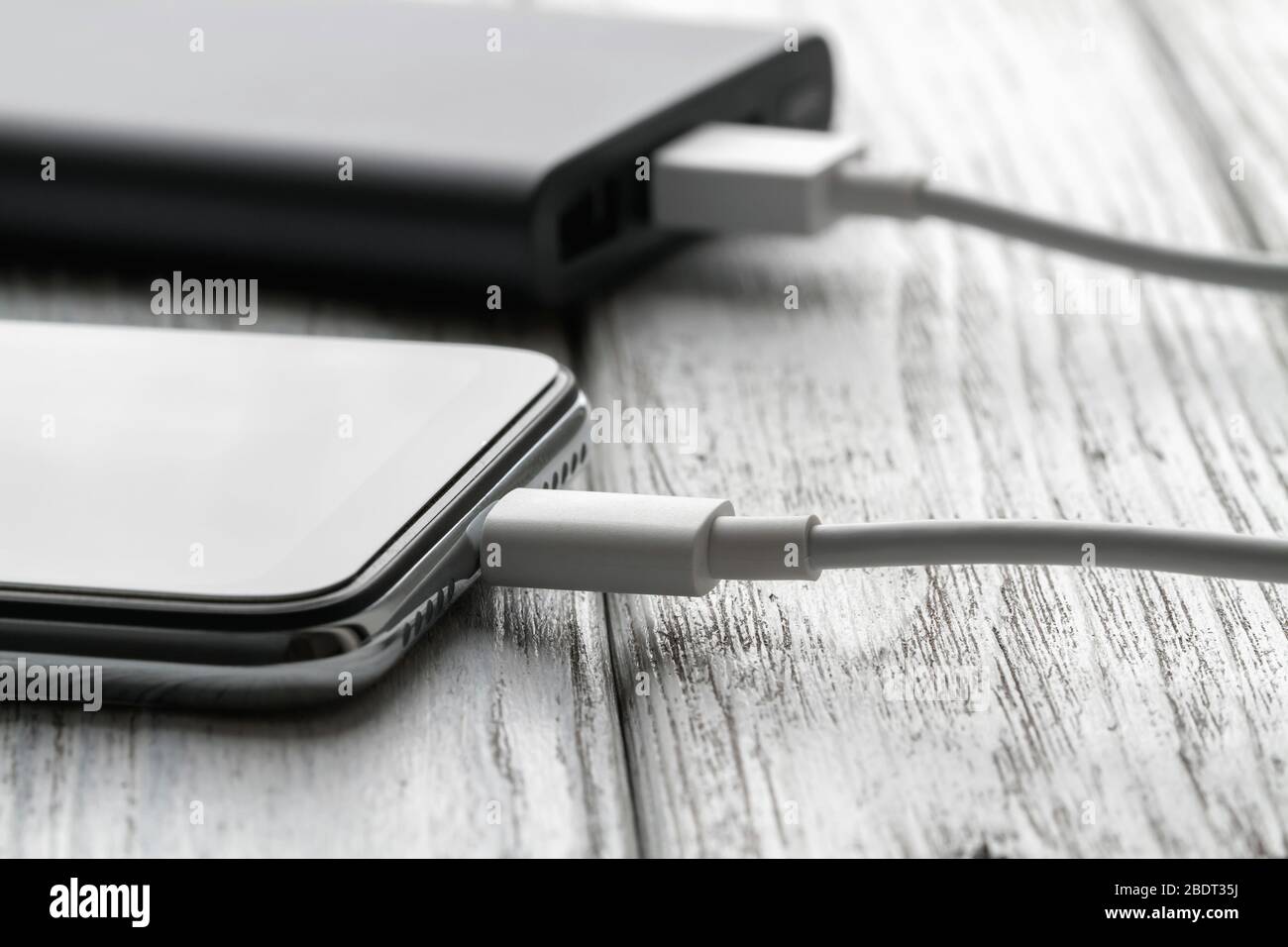 Lo smartphone si sta ricaricando dal powerbank esterno con un cavo su uno sfondo grigio di legno. Primo piano, messa a fuoco selettiva Foto Stock