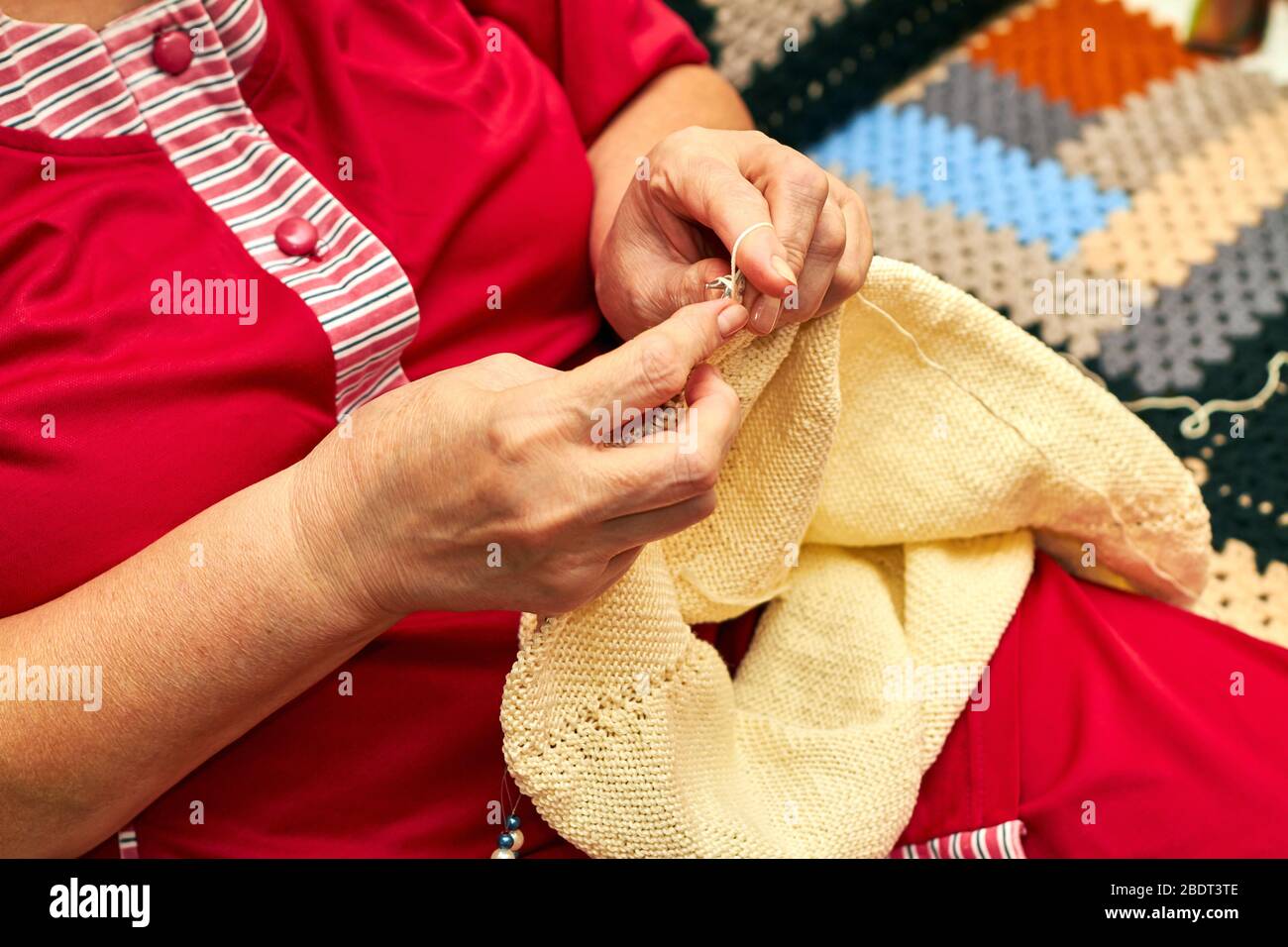 Donna è a maglia un maglione caldo beige. Una donna anziana si inginocchiò  sul divano. Un hobby di donna anziana è la maglieria Foto stock - Alamy