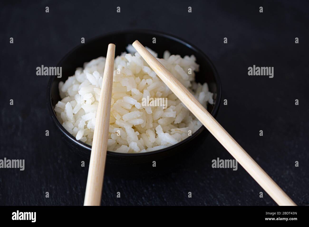 Recipiente per riso con bacchette cinesi su sfondo scuro Foto Stock