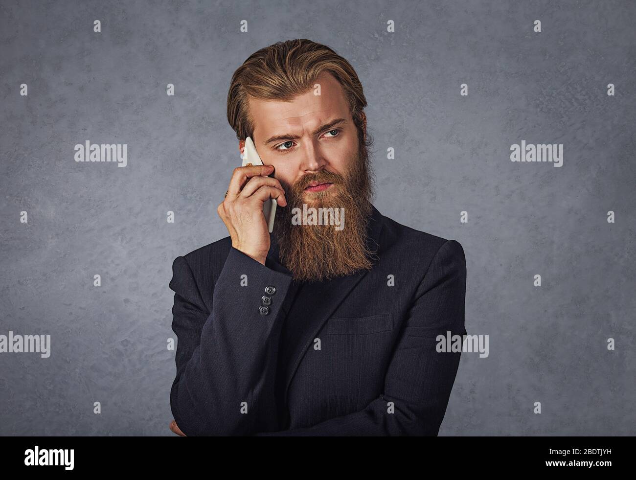 Giovane uomo fresco con barba camminare e parlare con il telefono cellulare isolato grigio parete di fondo Foto Stock