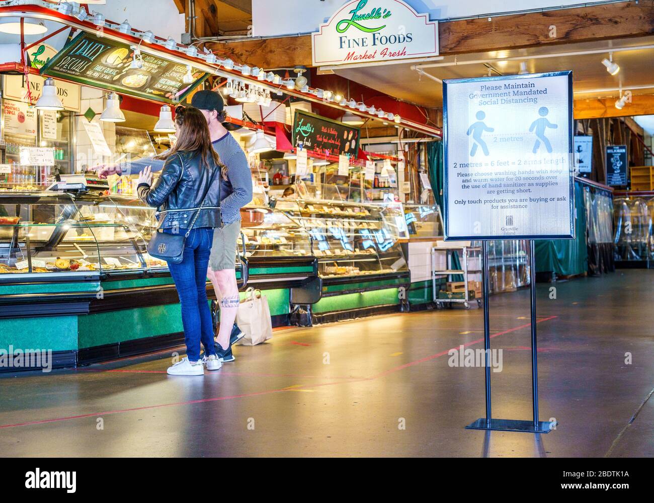 Vancouver, Canada - 7 aprile 2020: Coppia acquistare cibo take-out all'interno del mercato pubblico di Granville Island durante la pandemia di Coronavirus Foto Stock
