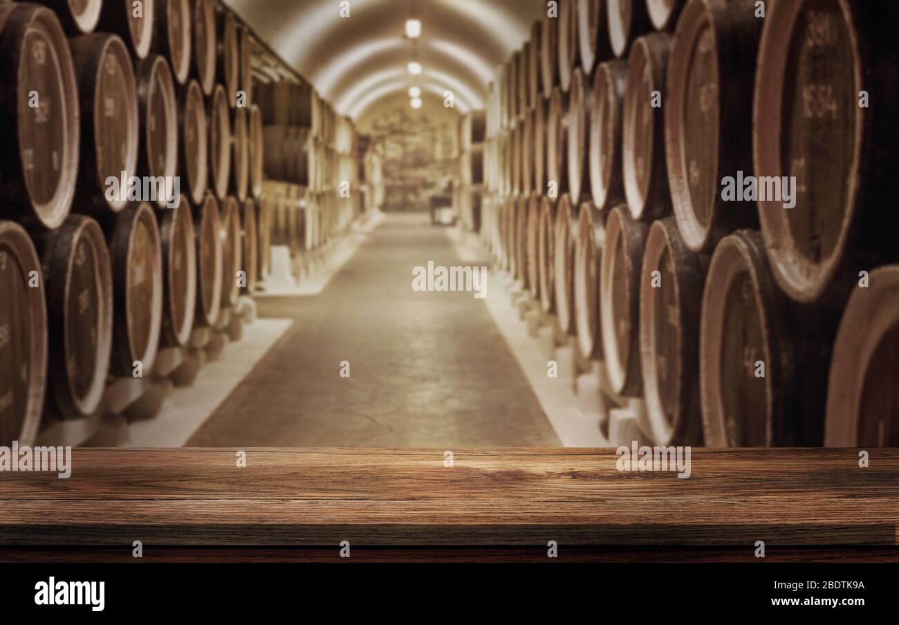 Tavolo vuoto in legno con sfondo sfocato di botti di vino nella volta del vino. Concetto di cantina e bevande. Rappresentazione 3D - Illustrazione. Foto Stock