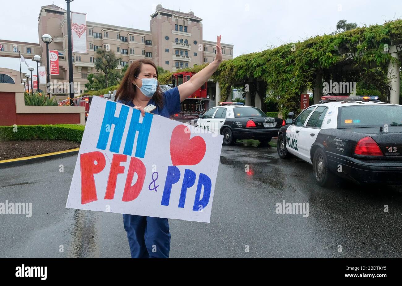 Los Angeles, California, Stati Uniti. 9 Aprile 2020. Un operatore sanitario in possesso di un cartello saluta mentre il personale della polizia e del reparto antincendio di Pasadena si accingono davanti all'Huntington Hospital con luci di emergenza e sirene attivate per mostrare apprezzamento agli operatori sanitari nella sala di emergenza e in tutto l'ospedale di Pasadena, California, giovedì 9 aprile 2020. Credit: Ringo Chiu/ZUMA Wire/Alamy Live News Foto Stock