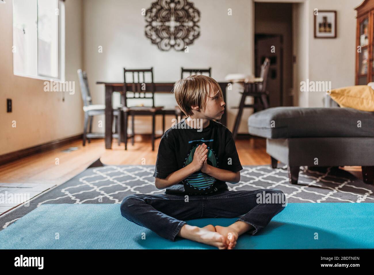 Ragazzo in età scolare che fa yoga in soggiorno durante l'isolamento Foto Stock