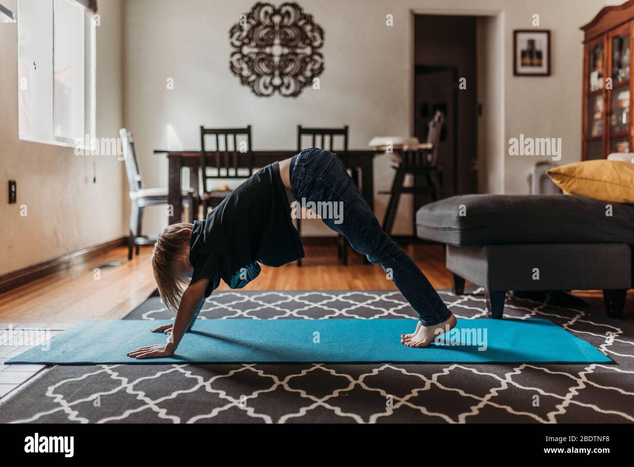 Ragazzo in età scolare che fa yoga in soggiorno durante l'isolamento Foto Stock