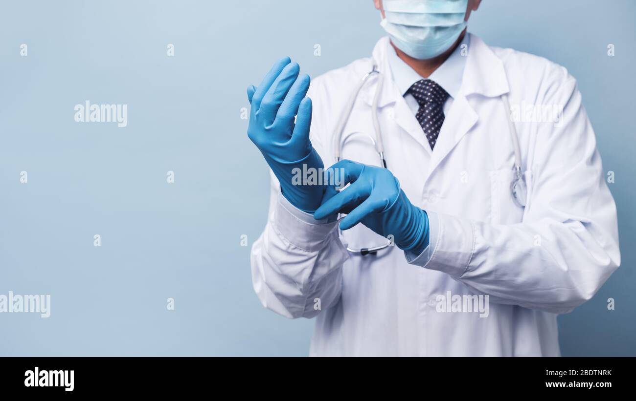 Un medico di sesso maschile in una maschera medica mette su guanti di gomma. Rimedi per infezione e coronovirus Foto Stock