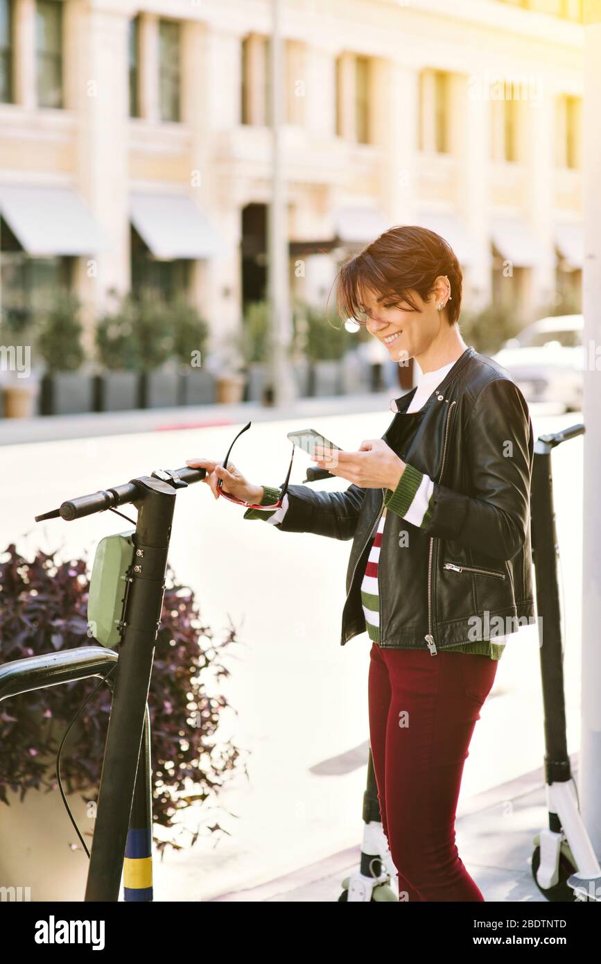 Donna millenaria in città, affitta uno scooter con il suo smartphone per spostarsi - Viaggi - Urbano - felice Foto Stock