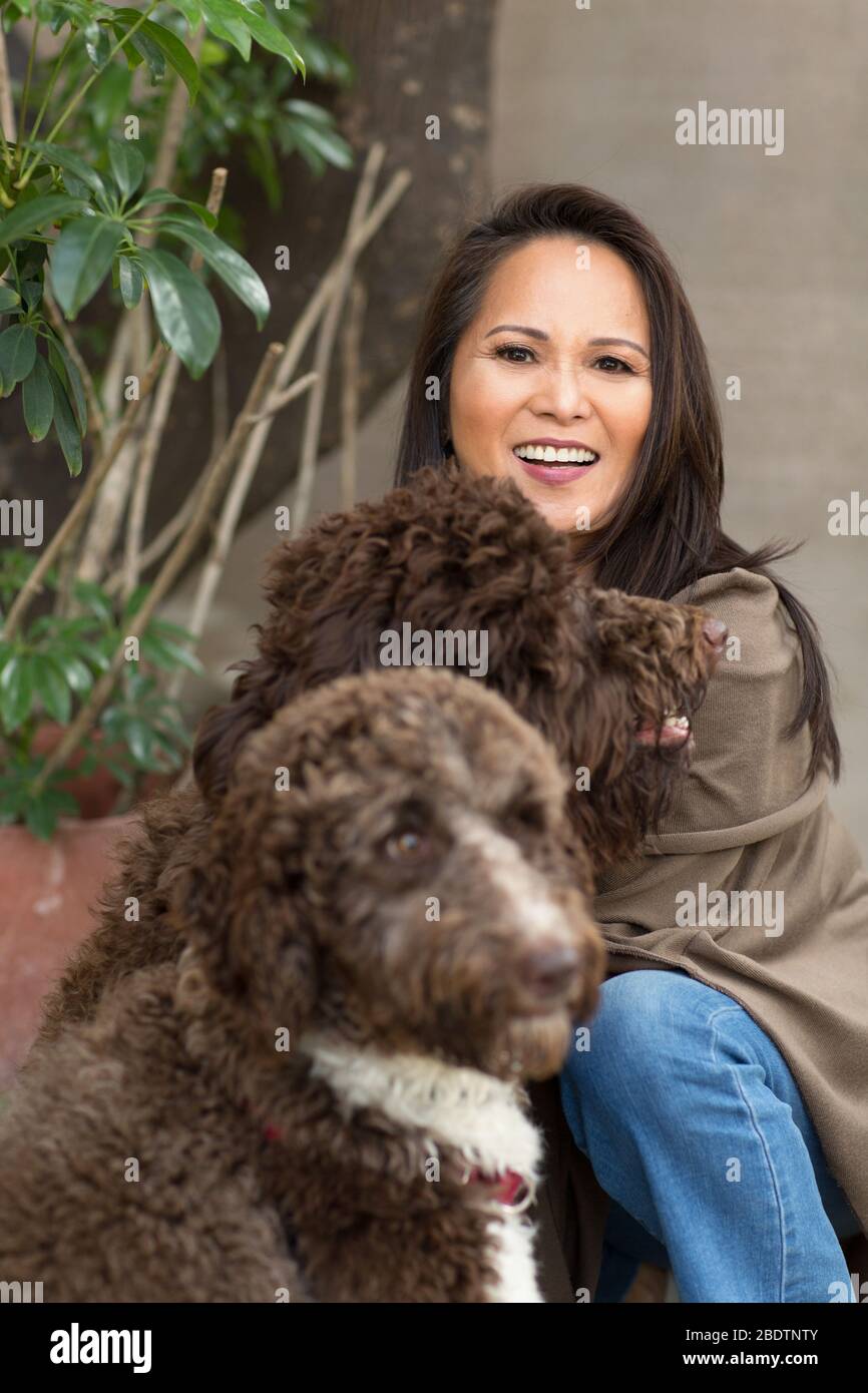 Donna asiatica matura ridendo e giocando con il suo cane. Foto Stock