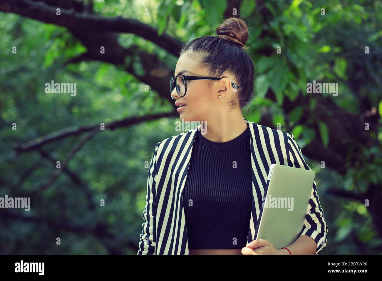 Studentessa donna in profilo che tiene un notebook che guarda di lato nel parco Foto Stock