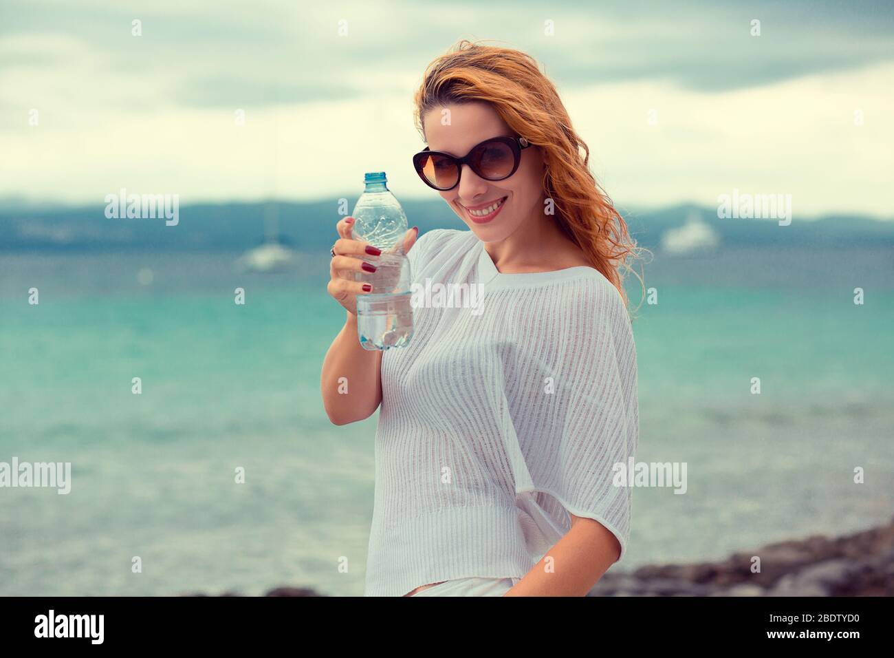 Bella giovane donna brunetta in occhiali da sole bere acqua e rinfrescarsi  dopo aver corso in spiaggia su uno sfondo di mare. Instagram filtro effetto  ap Foto stock - Alamy