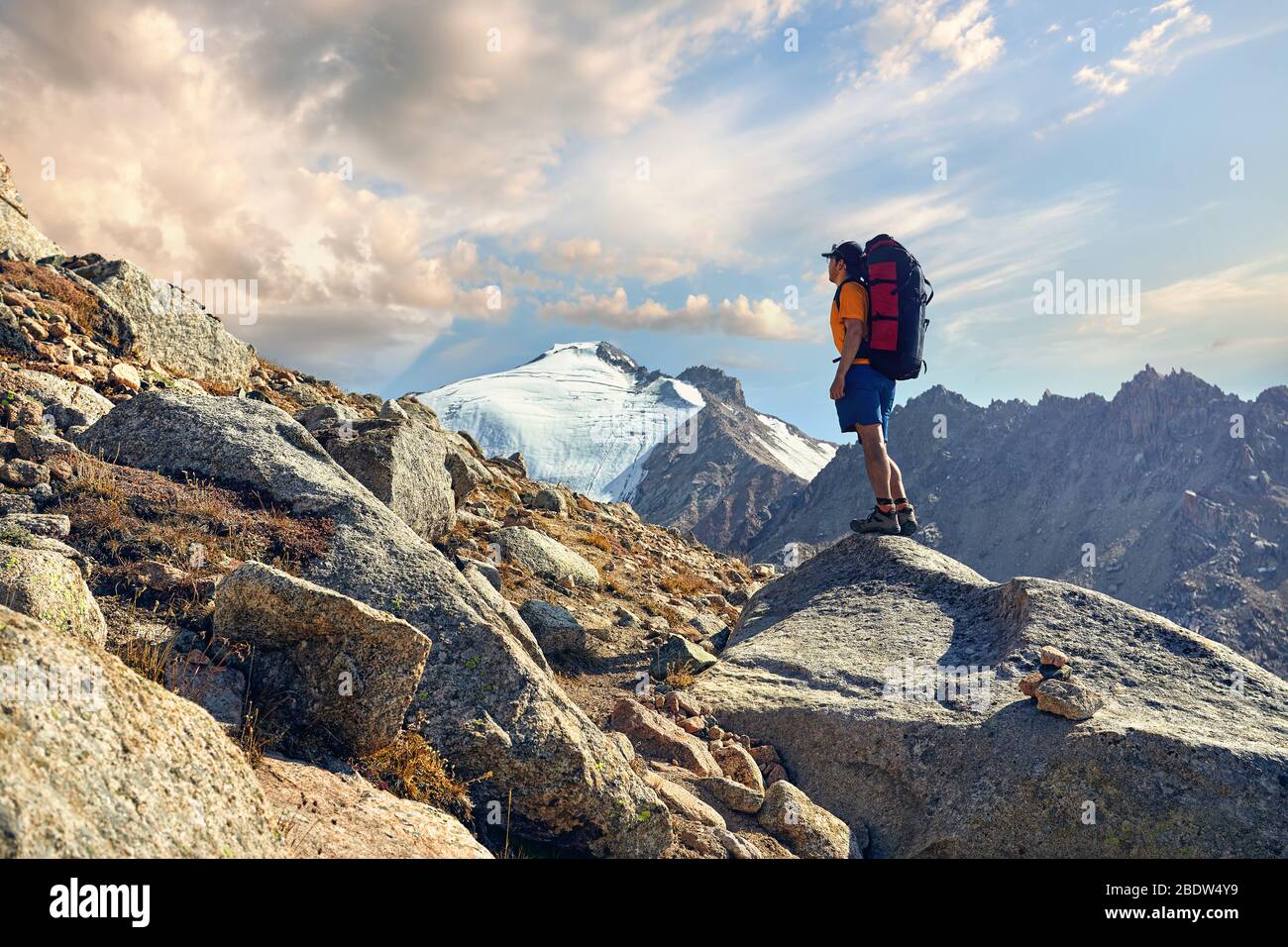 Escursionista in maglietta arancione con grande zaino cercando sul vertice nevoso a sfondo Foto Stock