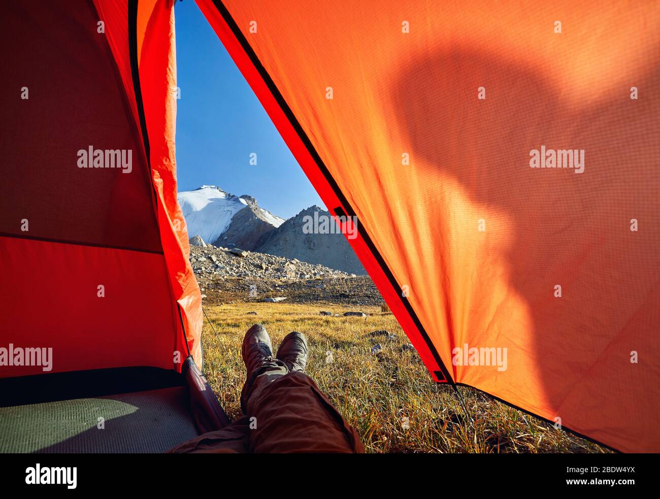 Escursionista gambe dalla tenda arancione con la vista bella vertice nevoso Foto Stock