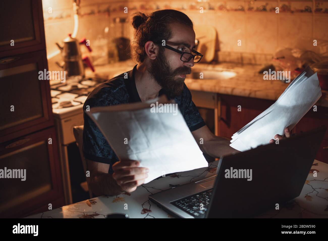 Stressato giovane hippster lunghi capelli bearded uomo sta controllando la fattura in kitchen.Invoice e finanza. Foto Stock