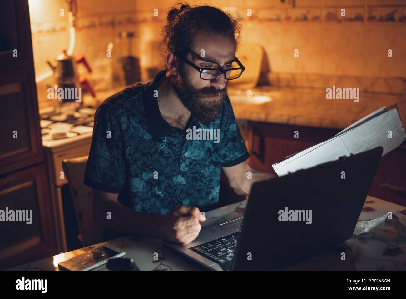 Stressato giovane hippster lunghi capelli bearded uomo sta controllando la fattura in kitchen.Invoice e finanza. Foto Stock