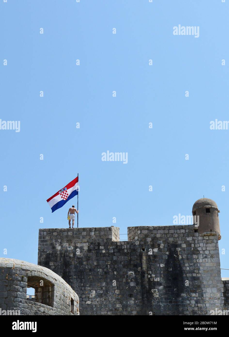 Un uomo che si erge accanto alla bandiera croata sulle mura della città vecchia di Dubrovnik, Croazia. Foto Stock