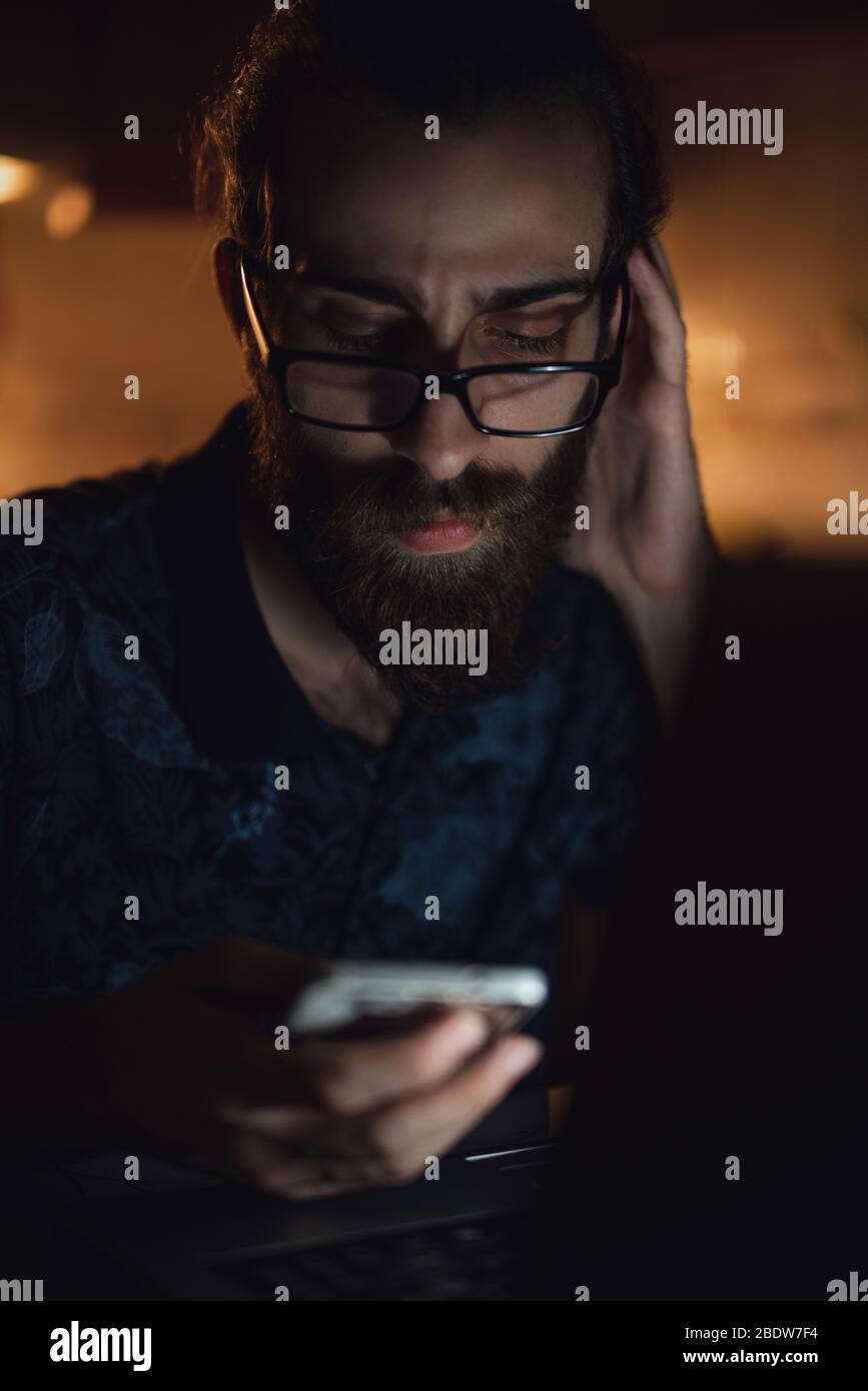 Stressato giovane hippster lunghi capelli bearded uomo sta controllando la fattura in kitchen.Invoice e finanza. Foto Stock