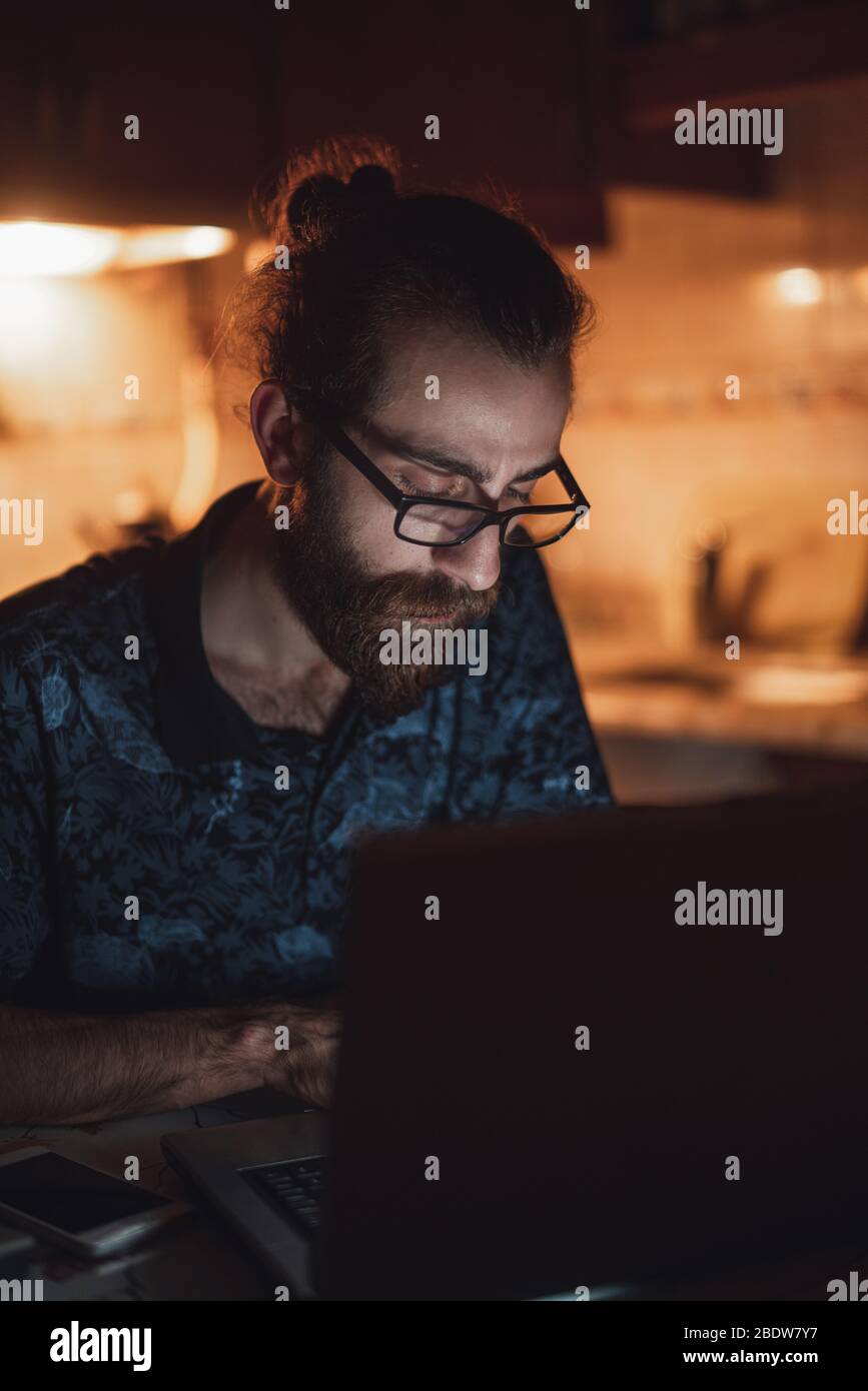 Stressato giovane hippster lunghi capelli bearded uomo sta controllando la fattura in kitchen.Invoice e finanza. Foto Stock