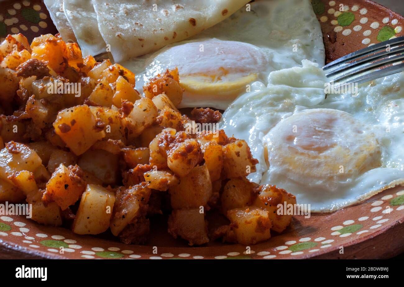 Su uova medie con patate e chorizo o huevos estrellados con papas y chorizo, su un piatto di fango messicano o argilla come parte di una colazione messicana. Foto Stock