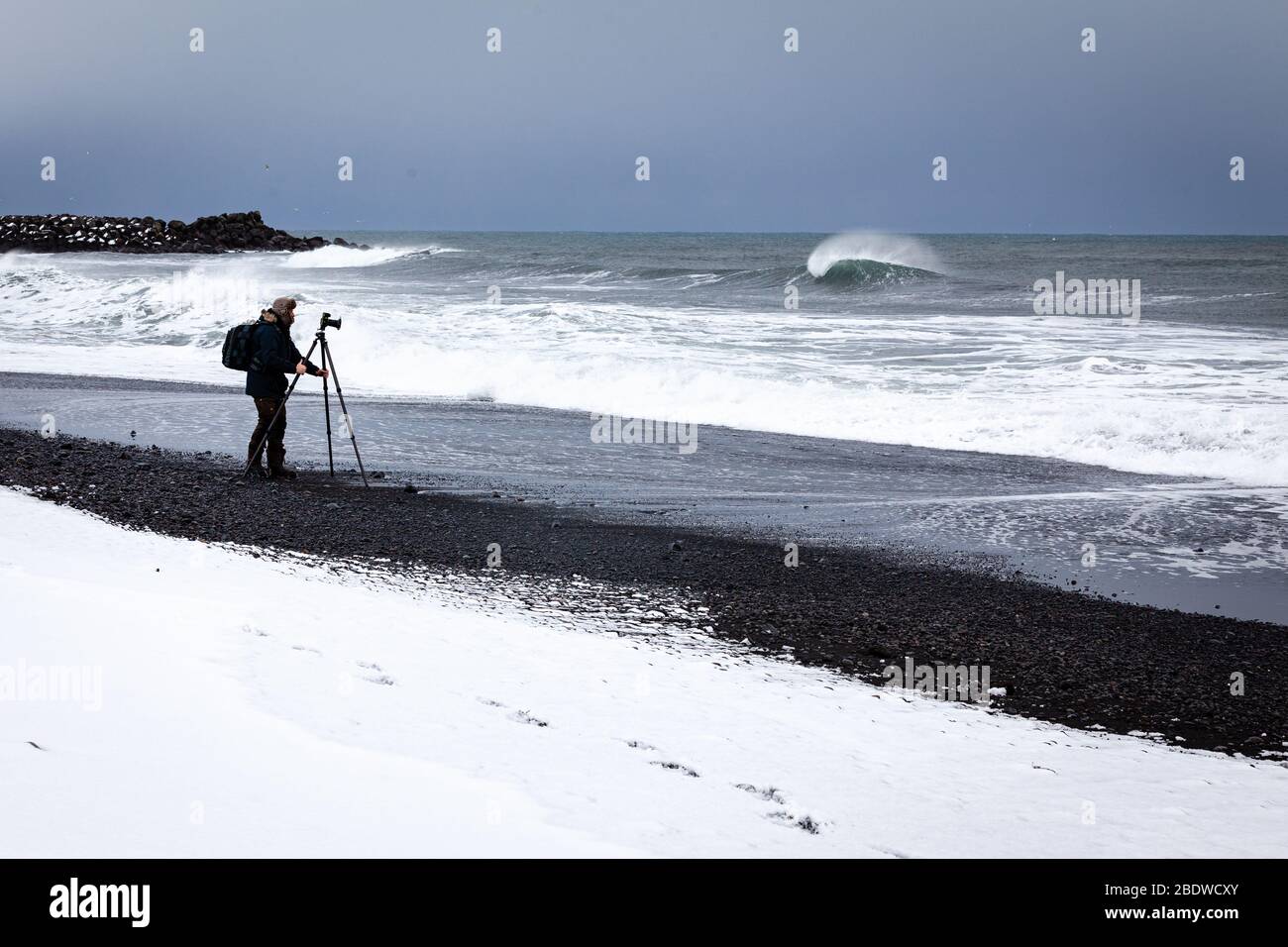 Un fotografo che fotografa il mare sulla famosa spiaggia di sabbia nera di Reynisfjara in inverno a Vík í Mýrdal, sulla costa meridionale dell'Islanda Foto Stock