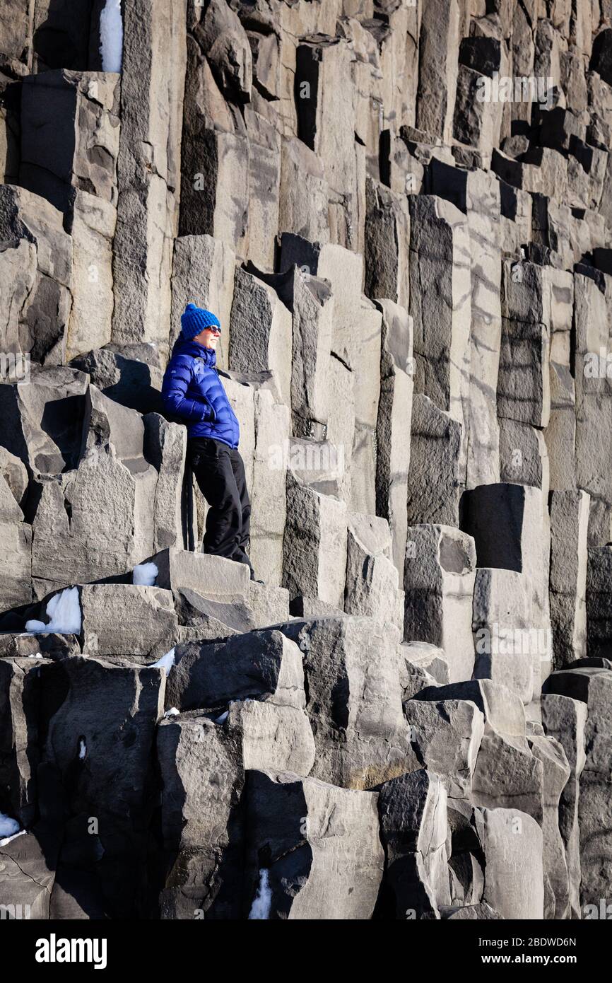 Una donna che si trova su colonne basaltiche a Reynisfjara spiaggia di sabbia nera in inverno vicino a Vík í Mýrdal, Islanda meridionale Foto Stock