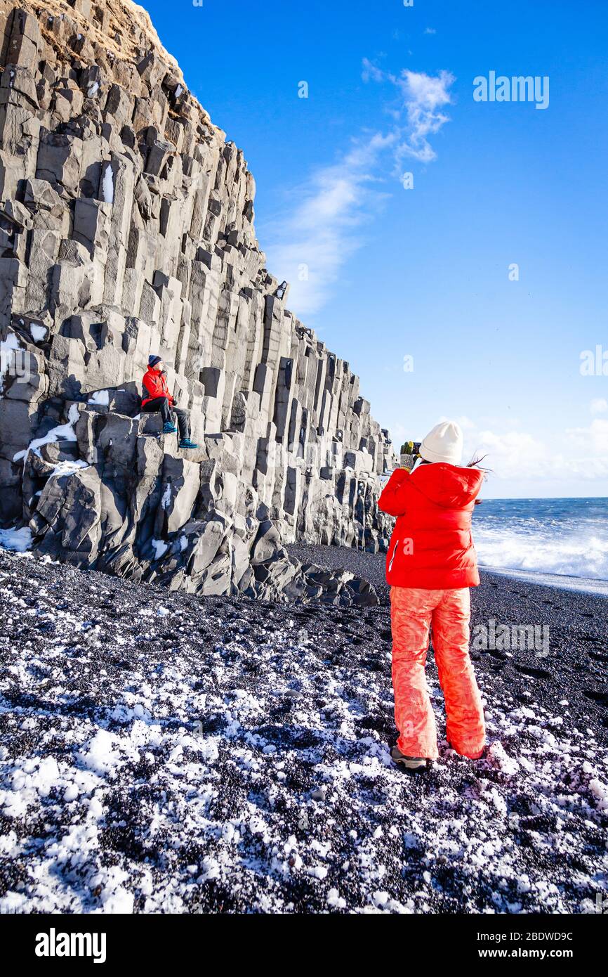 I turisti scattano foto alle colonne basaltiche della spiaggia di sabbia nera di Reynisfjara in inverno vicino a Vík í Mýrdal, Islanda meridionale Foto Stock
