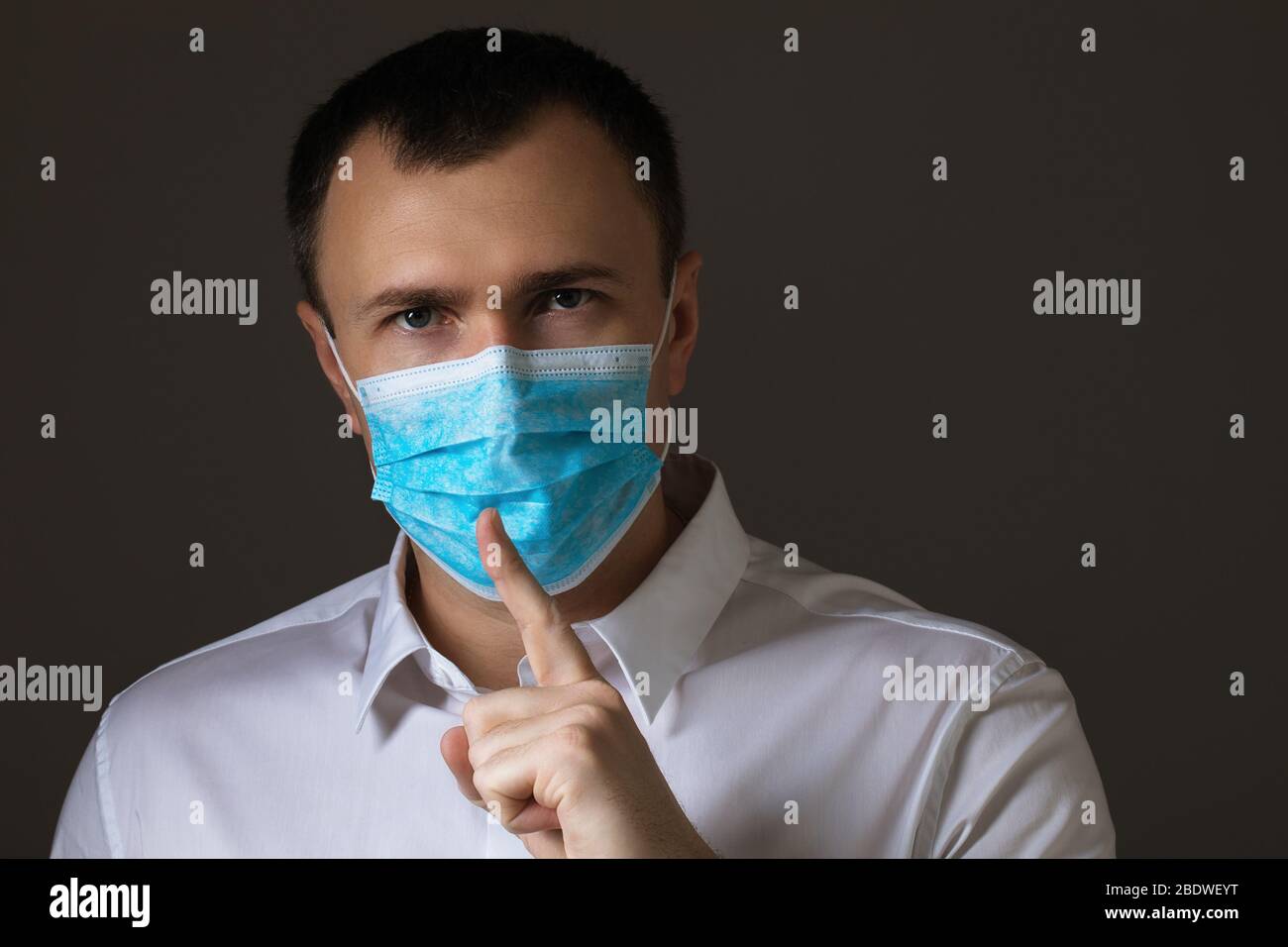 L'uomo mascherato mostra un segno di silenzio. Il concetto di coronavirus è una vera minaccia o un'isteria di massa Foto Stock