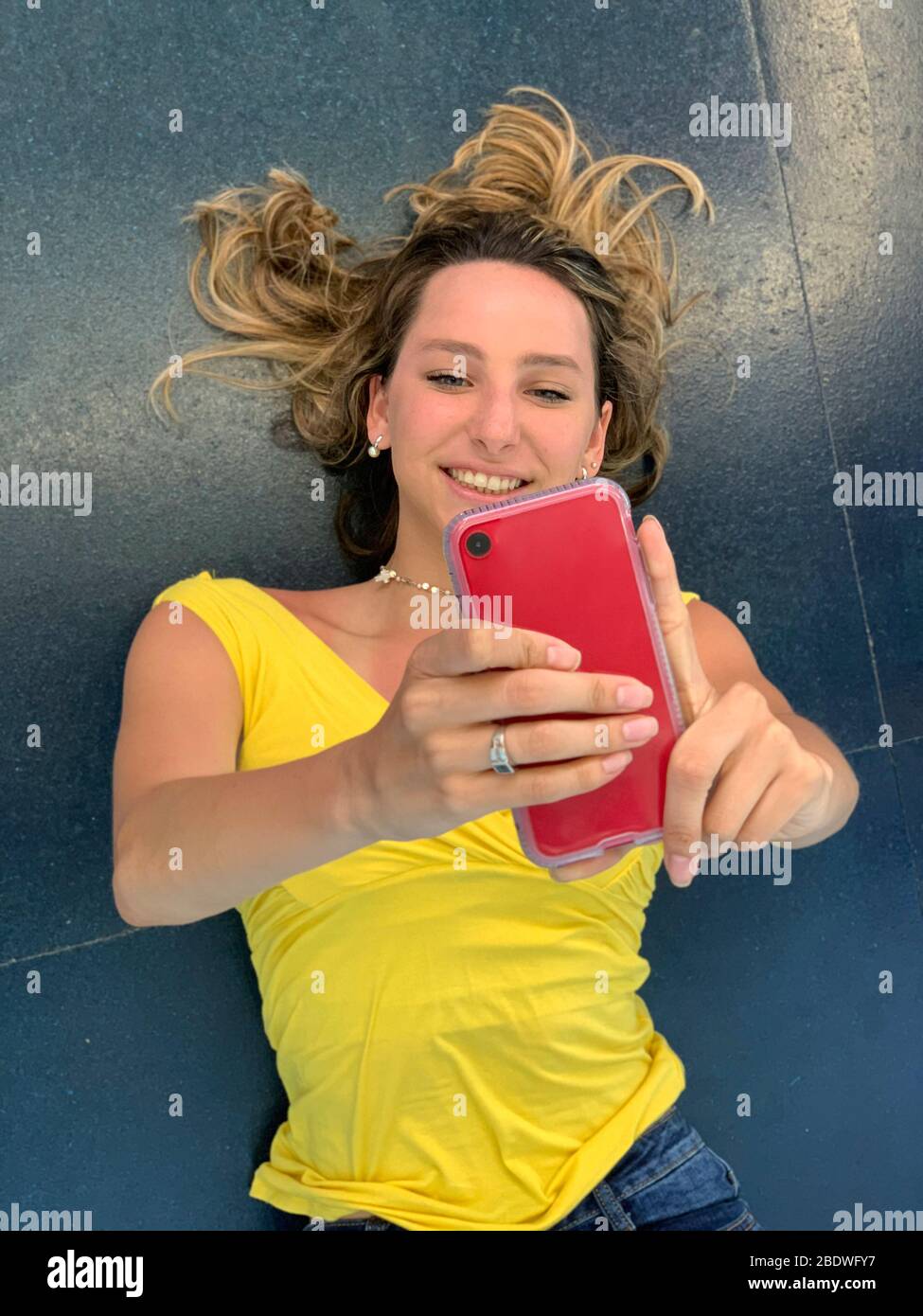 Giovane donna sdraiata sul pavimento prendendo selfie Foto Stock