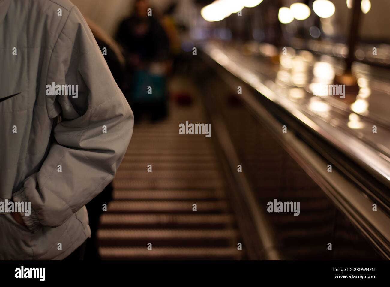 Il corpo di un uomo in una giacca su una scala mobile nella metropolitana con spazio per le copie. Scarsa illuminazione con sfondo sfocato Foto Stock