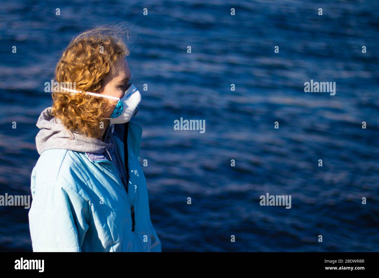 Vista laterale della ragazza che guarda di lato. Foto del profilo. Maschera respiratore donna in faccia per la protezione contro le malattie infettive e i virus. Blu scuro Foto Stock