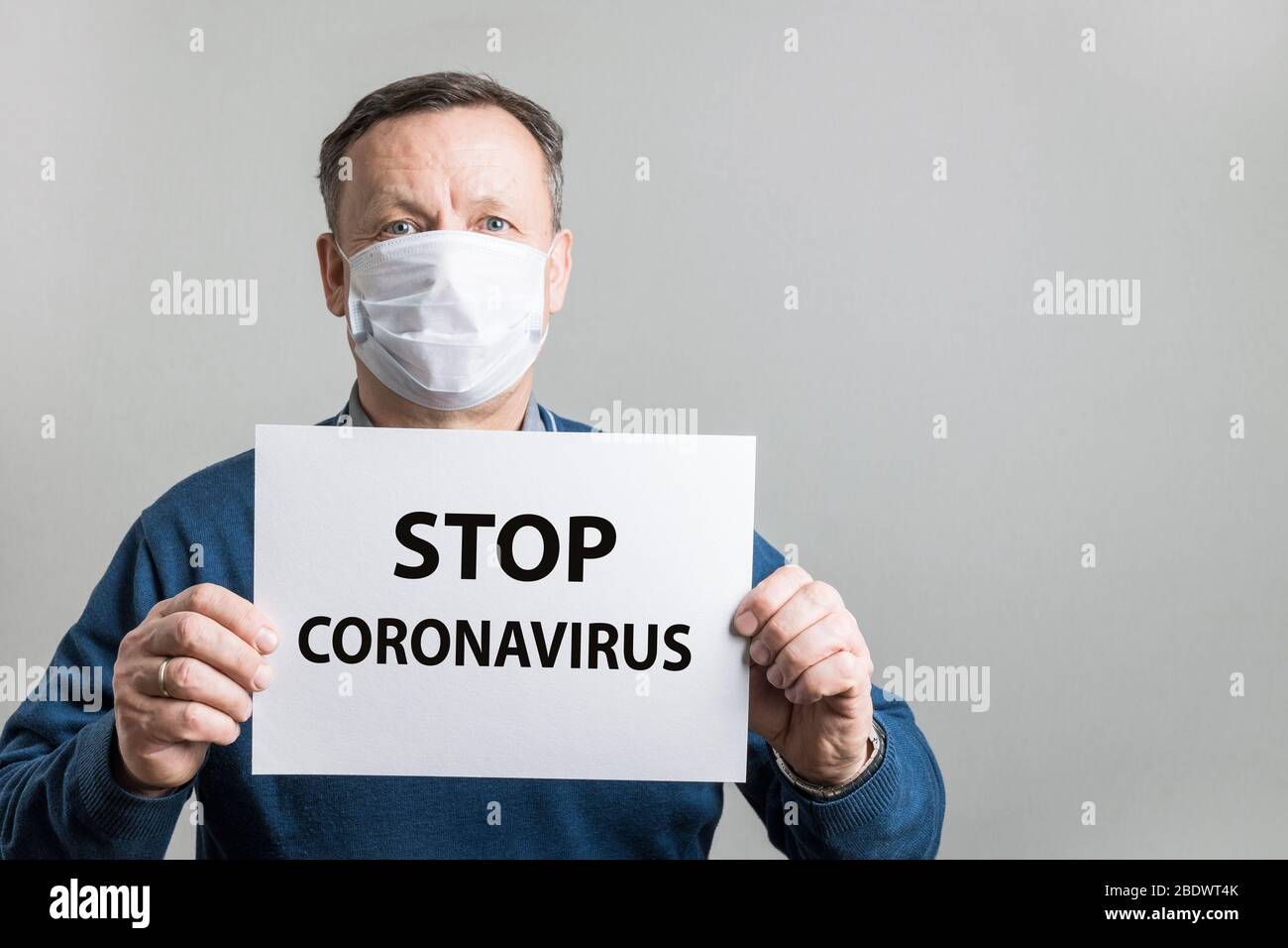 Uomo adulto in maschera medica protettiva che tiene bianco vuoto con testo - Stop Coronavirus. Covid-19. Quarantena. Rimani a casa. Foto Stock