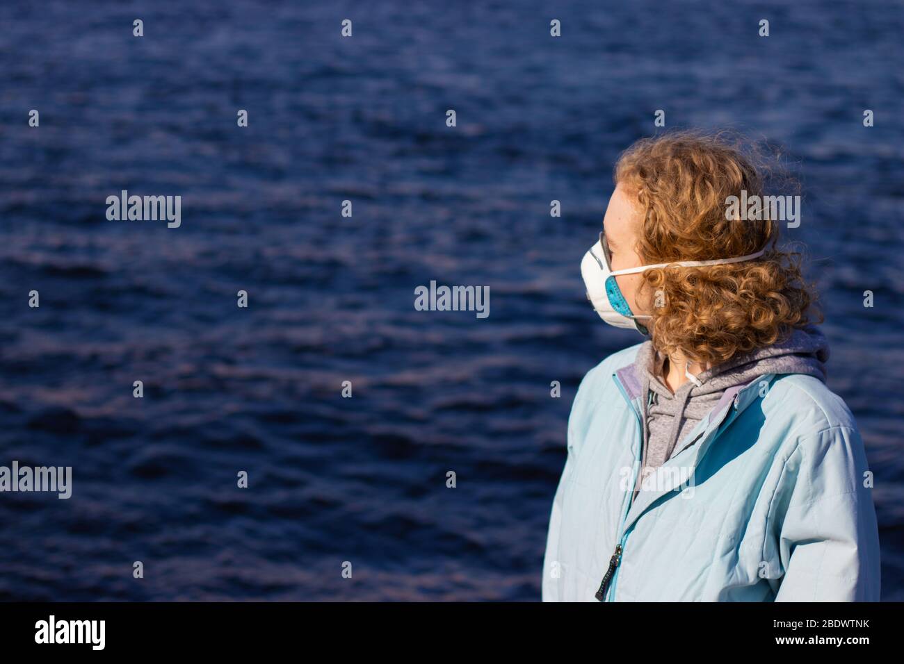 Donna bionda in medico facciale respiratore maschera vista laterale su sfondo sfocato con acqua. Spazio per la copia del testo relativo al problema sanitario Foto Stock