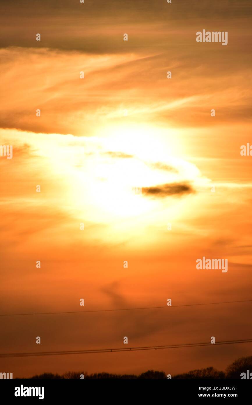 impostazione del sole tramonta in una striscia di formazioni nuvolose di colore rosso e arancione che danno un aspetto unearthly. Foto Stock