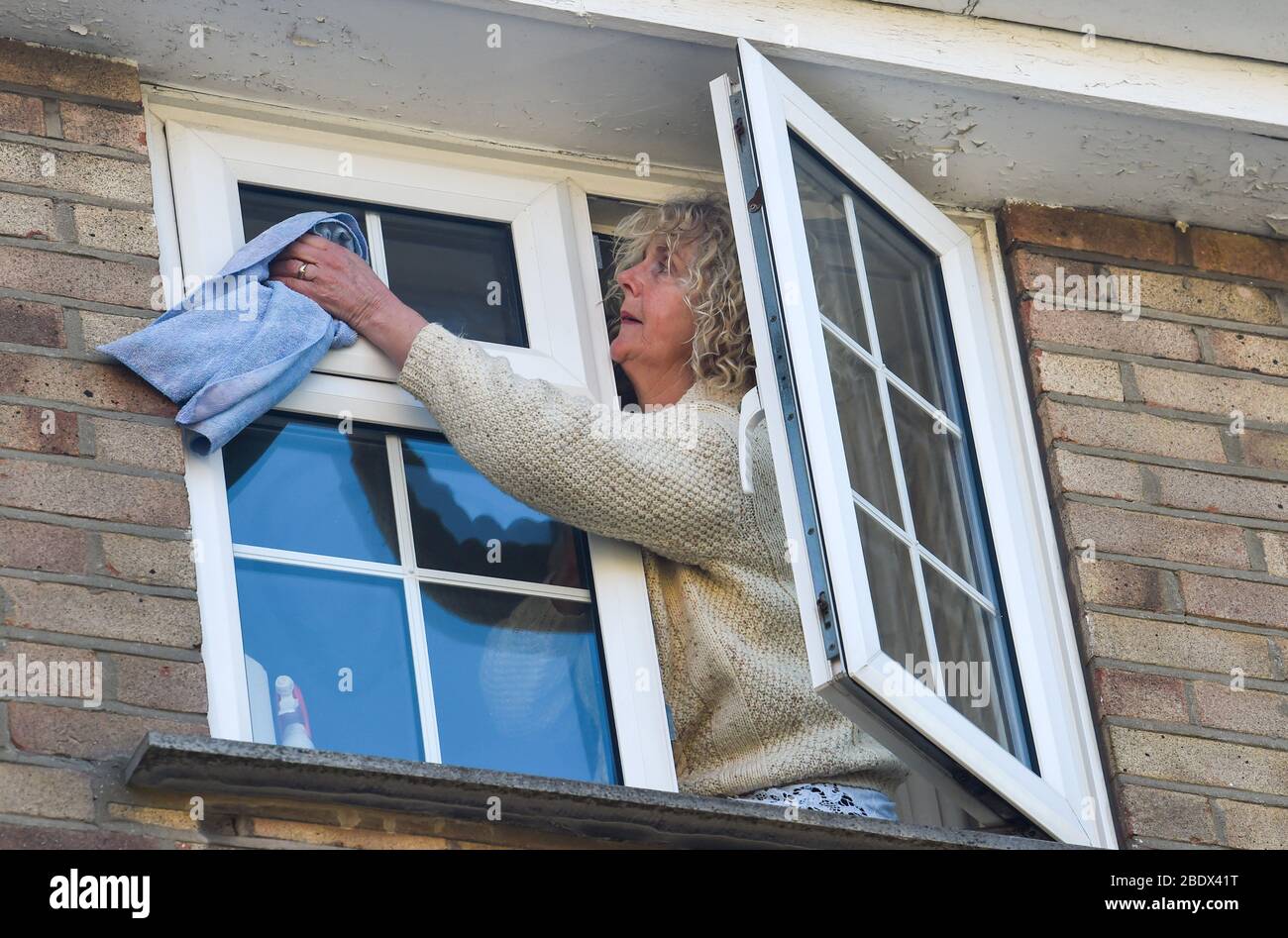 Donna matura si appoggia fuori dalla sua finestra per pulirli in primavera Regno Unito Foto Stock