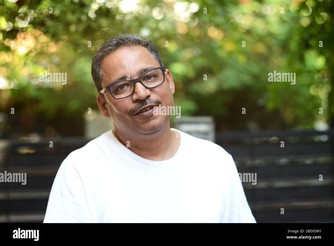 Uomo indiano che indossa una t-shirt bianca contro uno sfondo di natura sfocata Foto Stock