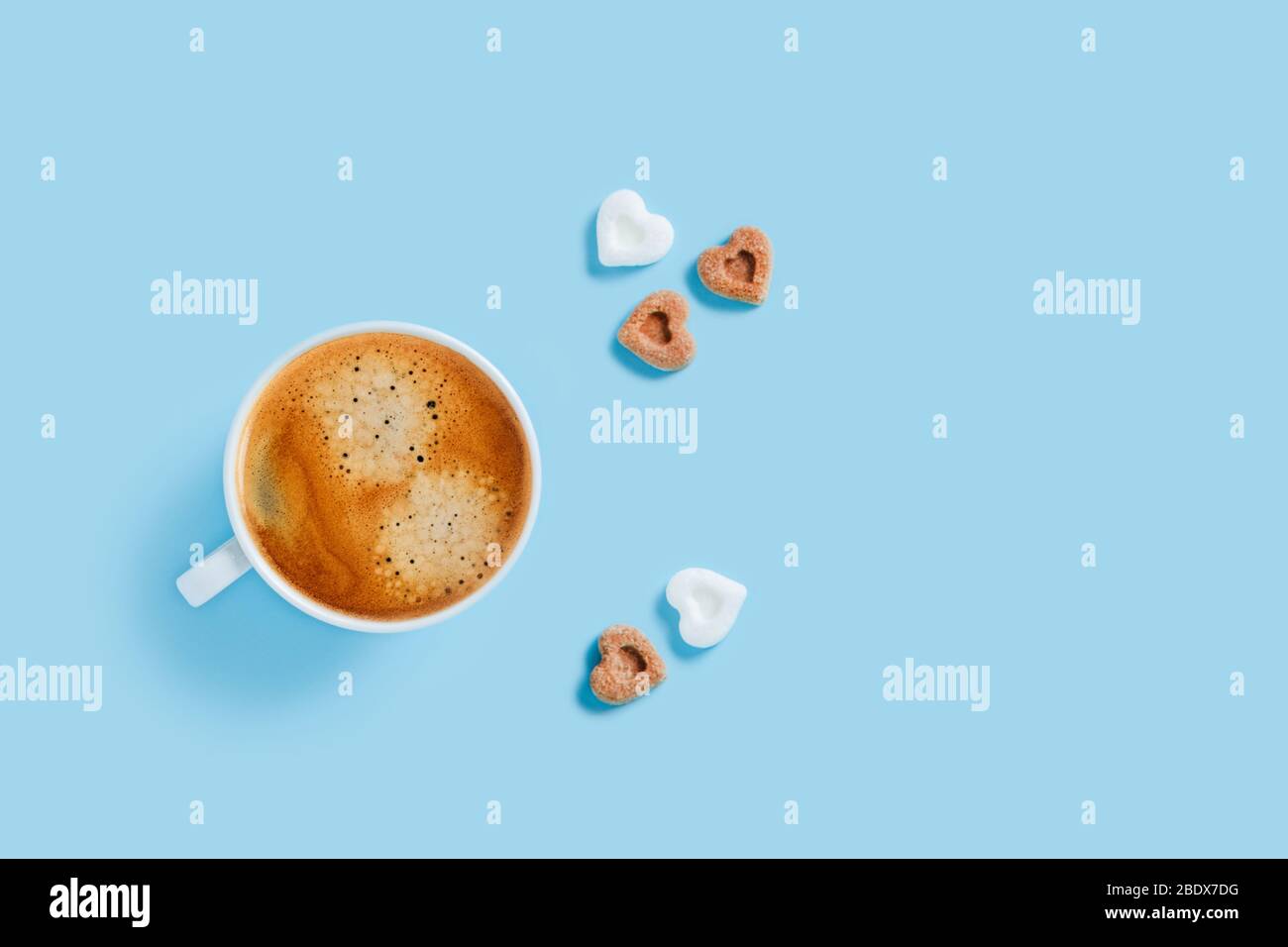 Tazza del mattino di caffè forte con cinque pezzi di zucchero a forma di cuore su sfondo blu. Foto Stock