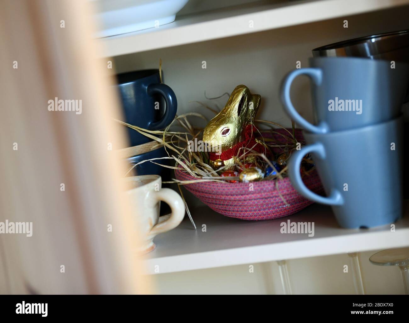 10 aprile 2020, Baviera, Garmisch-Partenkirchen: ILLUSTRAZIONE - un nido pasquale con coniglietto di cioccolato e uova di cioccolato è nascosto in un appartamento tra i piatti nel mobile. Foto: Angelika Warmuth/dpa Foto Stock