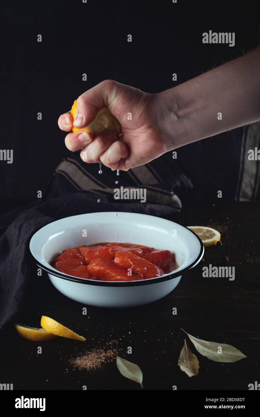 Salatura di pesce rosso. La mano maschile spreme un limone in una ciotola con salmone. Foto Stock