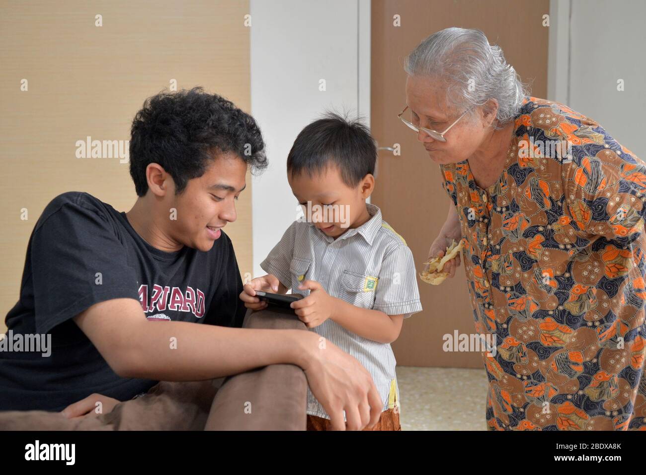Un ragazzo gioca con lo smartphone mentre suo fratello e sua nonna guardano. Foto Stock