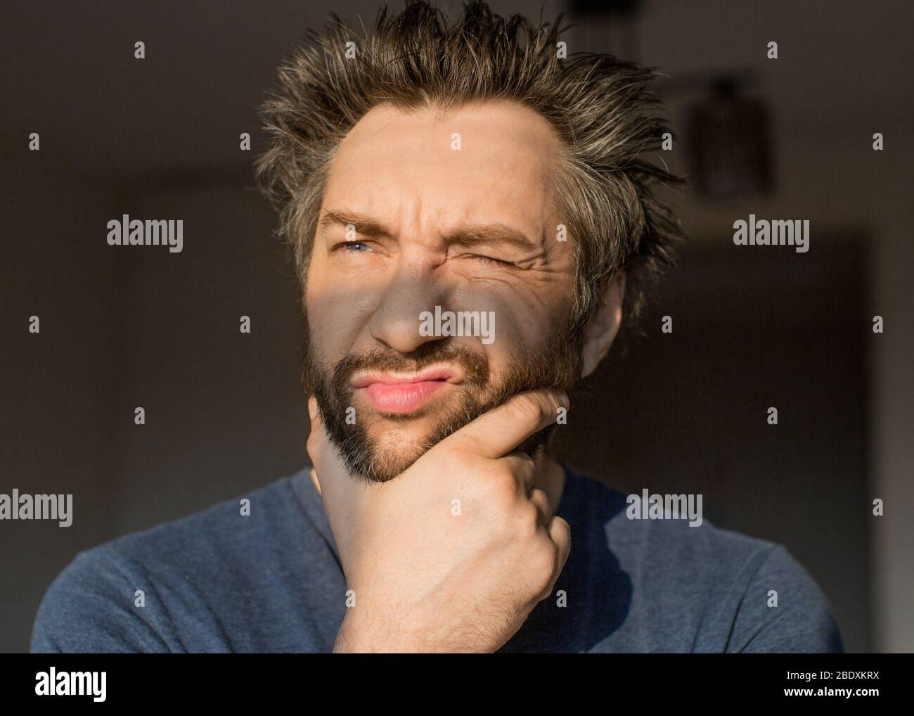 Uomo divertente dopo aver svegliato graffia la barba, guardando il sole del mattino. Chiudi verticale. Foto Stock