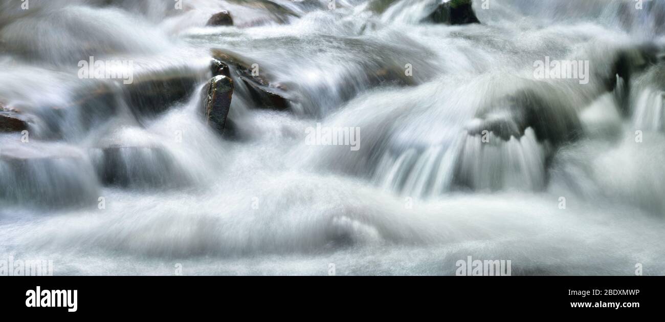 Ruscelli d'acqua splendidamente a cascata lungo un piccolo fiume selvaggio, formato panoramico e lunga esposizione per il flusso astratto Foto Stock
