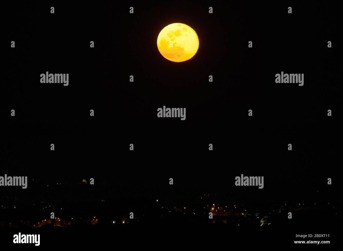 luna piena rossa nel cielo scuro e le luci della città Foto Stock