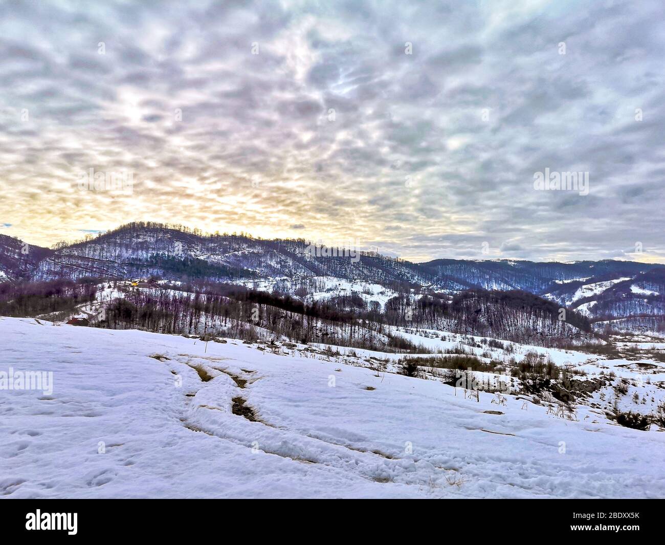 Paesaggio montano panoramico con piste innevate, cime innevate e nuvole illuminate dal tramonto sui Monti Carpazi della Romania, beau Foto Stock