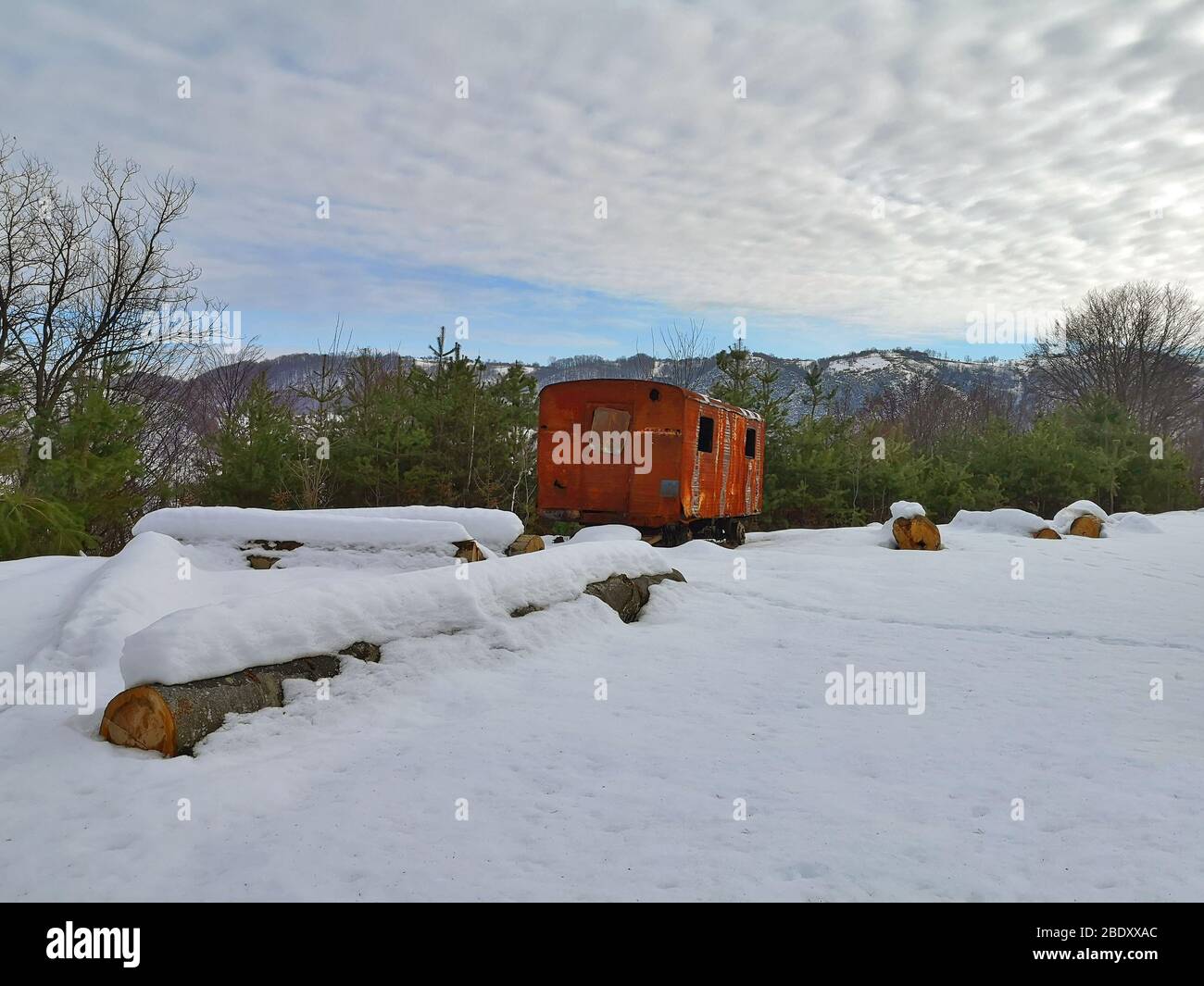 Paesaggio invernale da qualche parte nei Carpazi, in una radura di una foresta sempreverde vi è un vecchio carro ferroviario arrugginito, abbandonato circondato b Foto Stock