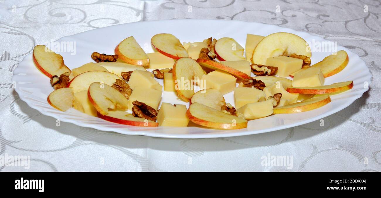 Piatto fresco con un mix di pezzi di formaggio cheddar, fette di mela e noci da parete preparato e sistemato su piatto bianco per una degustazione, piatto degustazione di formaggio w Foto Stock
