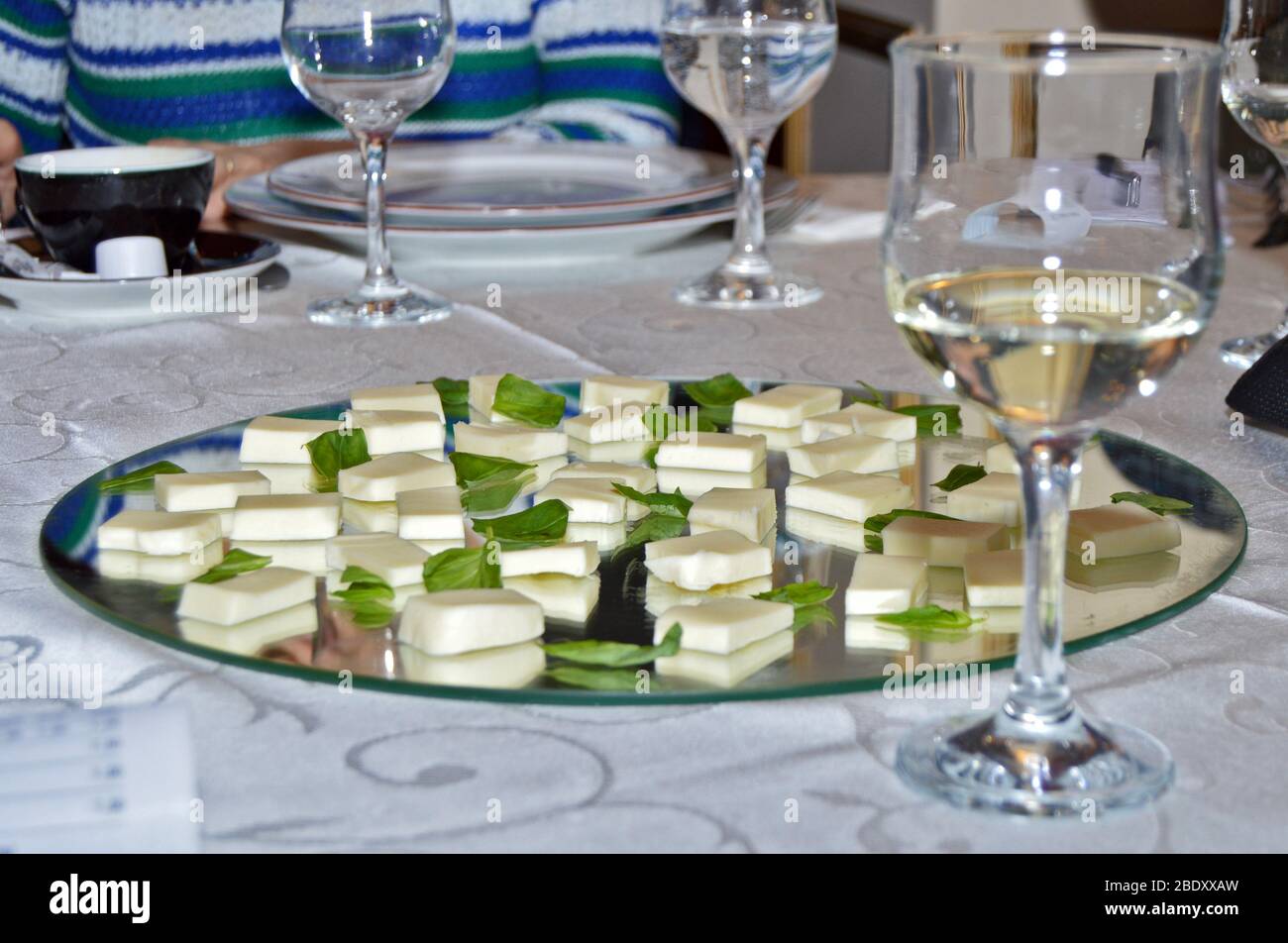 Ambiente elegante al tavolo del ristorante, primo piano di bicchieri di vino bianco pronti per la degustazione accanto al piatto a specchio con fette di mozzarella fresca Foto Stock