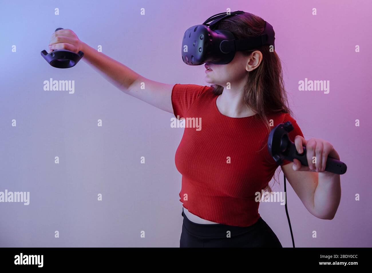 Una donna dai capelli castani in una giacca rossa gioca in realtà virtuale. La camera è piena di colori neon Foto Stock