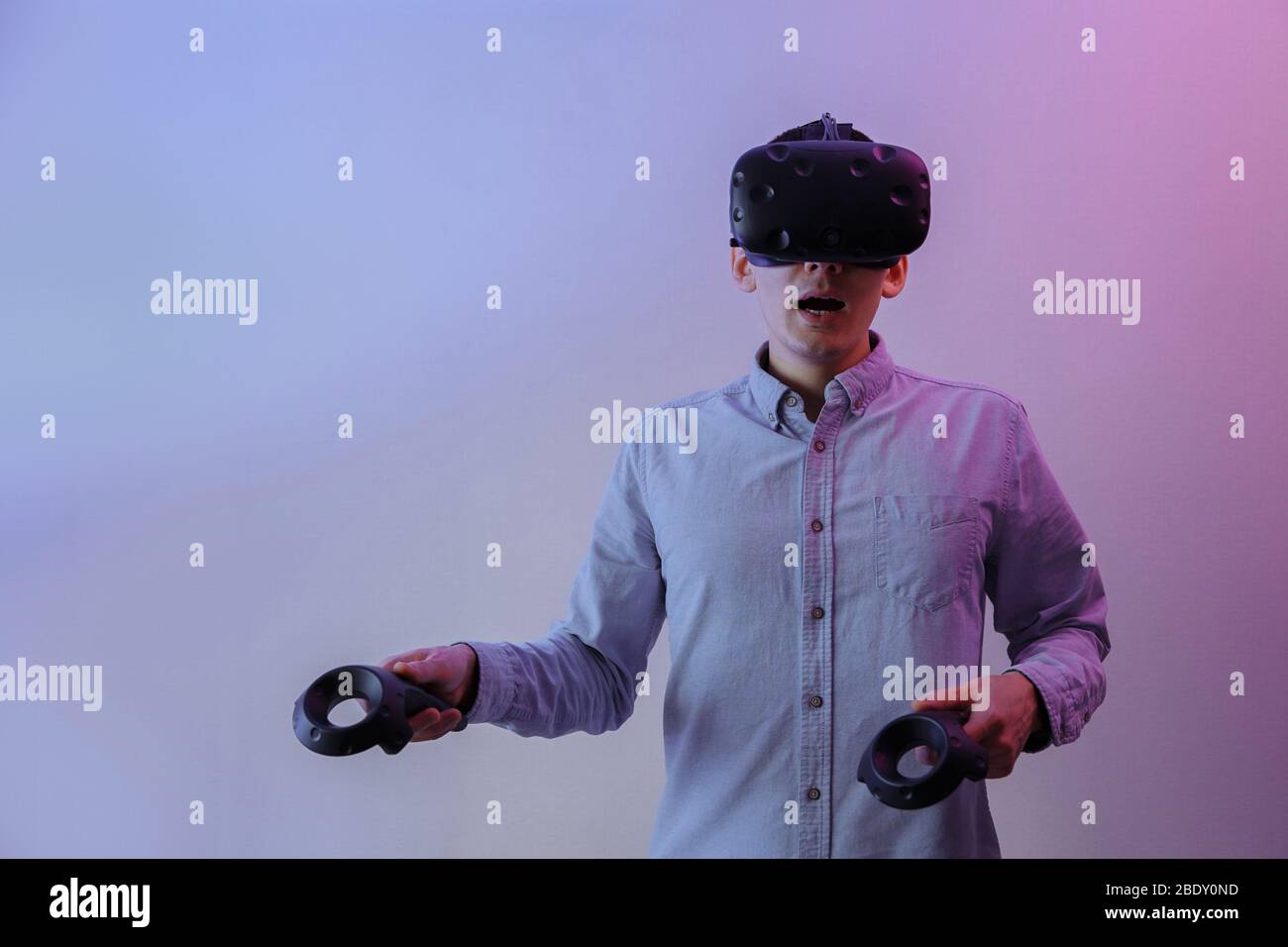 Un uomo in occhiali di realtà virtuale con gamepad nelle sue mani padroneggia la realtà virtuale. Un uomo è illuminato da una luce al neon. Foto Stock