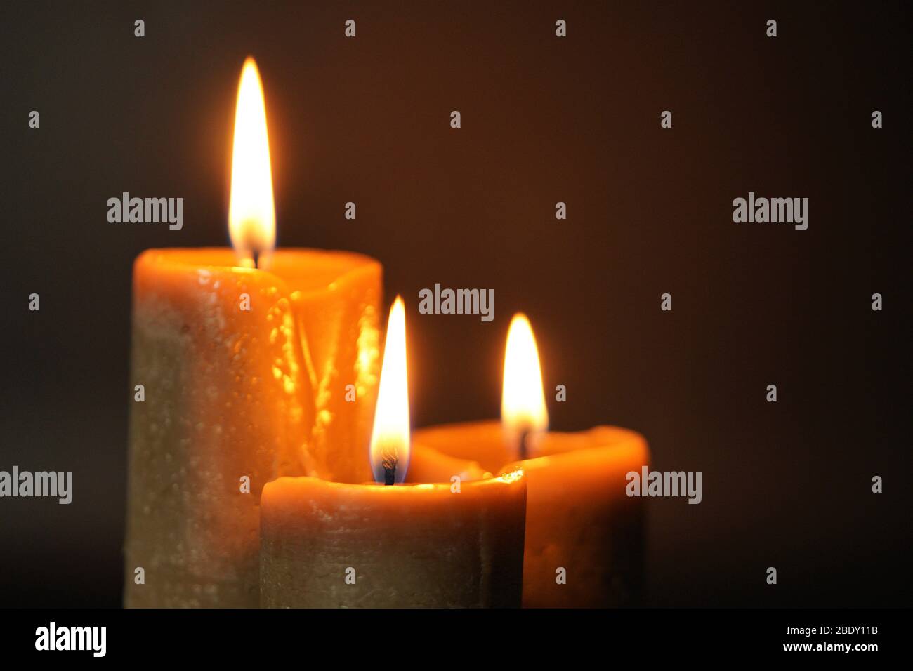 Gruppo di tre candele brune che bruciano su uno sfondo nero primo piano. Concetto di comfort, romanticismo, mistico, occultismo, religione, un simbolo di memory.Copy Foto Stock