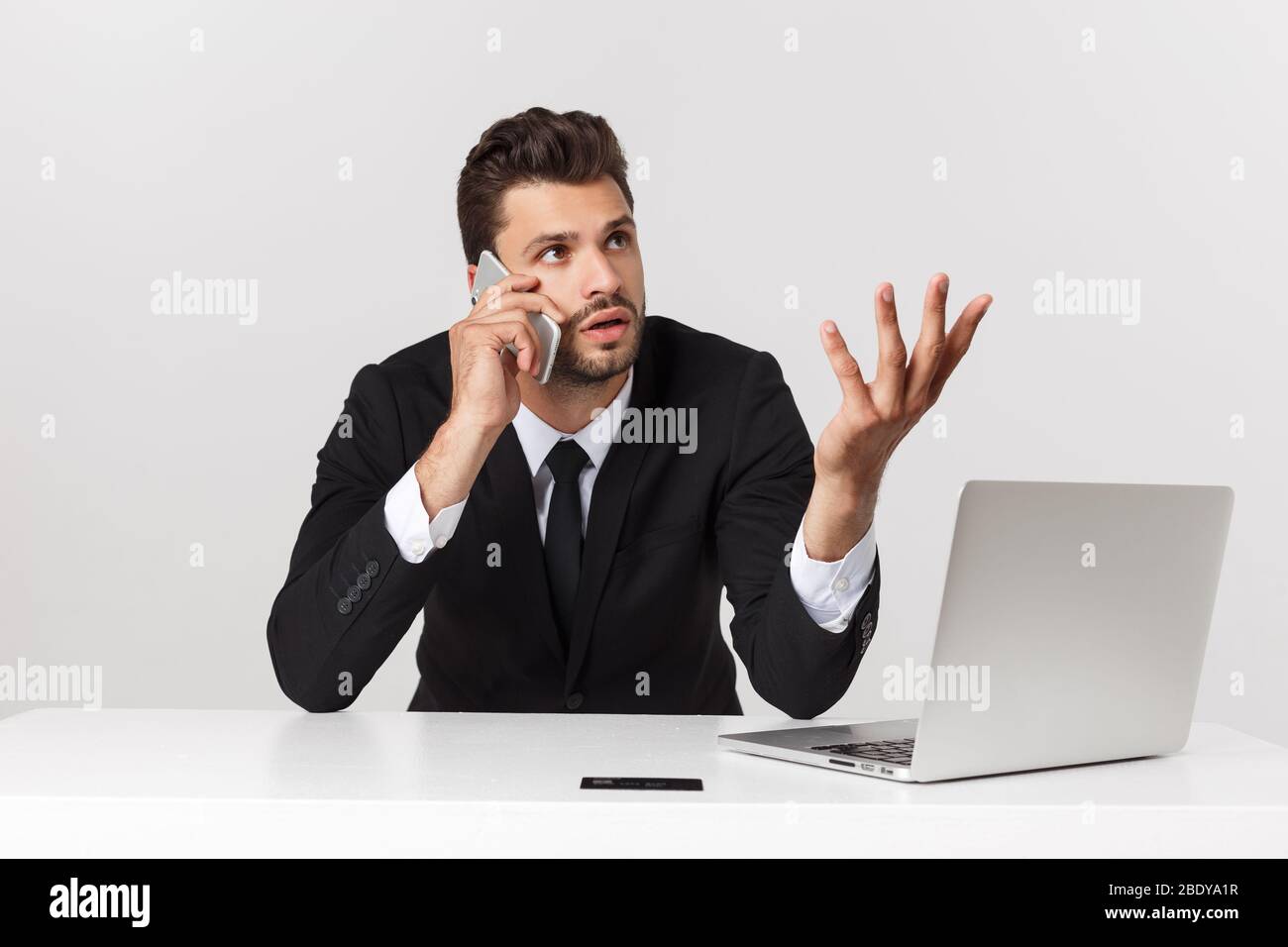L'attraente imprenditore caucasico preoccupato e stanco parlare sul telefono cellulare seduto alla scrivania dell'ufficio che lavora in stress ha funzionato eccessivamente e frustrato. Foto Stock