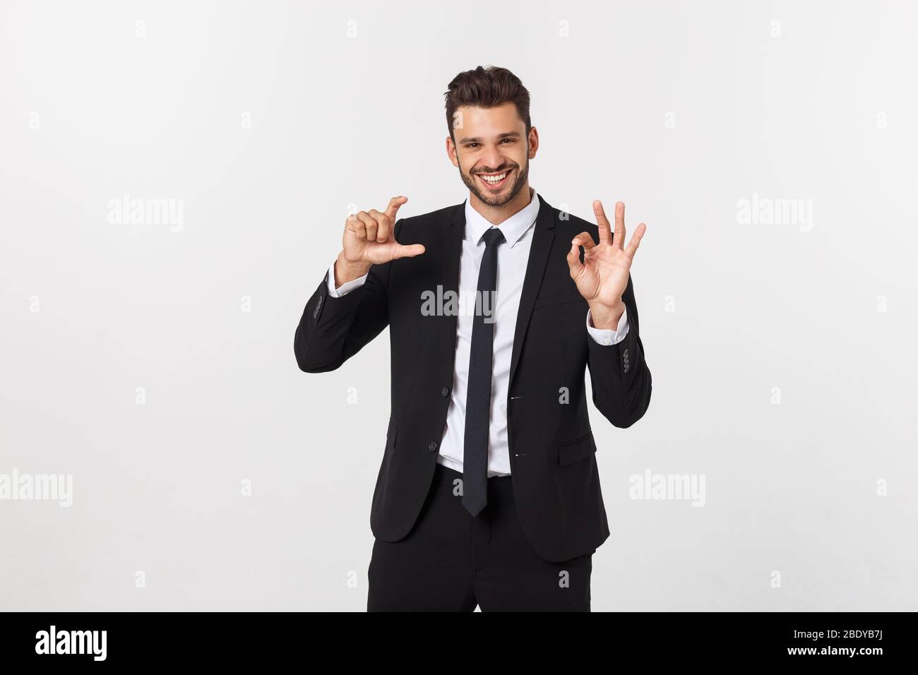 Un uomo d'affari fiducioso e di successo con abito nero e baffi. In un vestito mostra un segno di consenso e consiglia un prodotto o un servizio Foto Stock